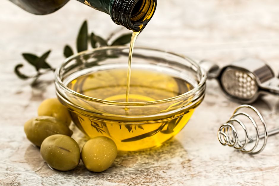 Χρυσαφένιο ελαιόλαδο που χύνεται σε μπολ, με ελιές δίπλα